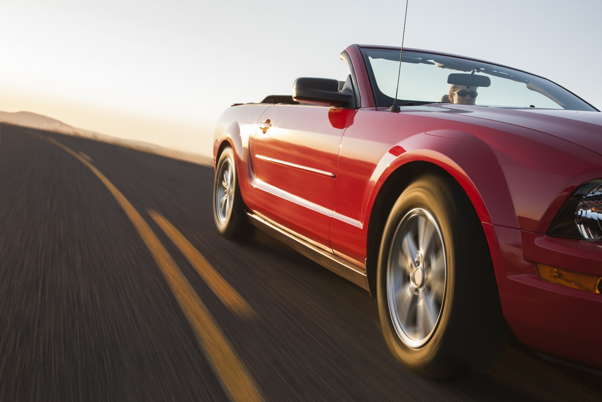 A low angle view of a convertible sports car moving on a highway late in the day.